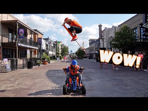 Child on a blue pedal go-kart rides toward the camera while another rider jumps a scooter high above them; large WOW graphic on the right.