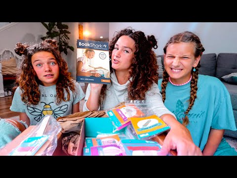 Three girls sit on a living room floor unboxing a BookShark homeschool kit, catalog visible.