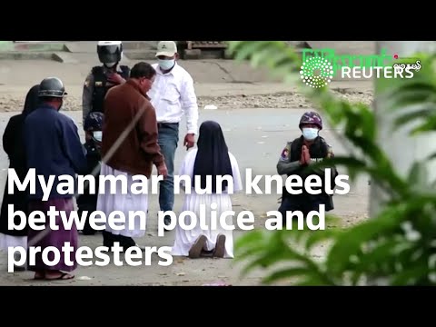警察とデモ隊の間で跪くミャンマーの修道女 (Myanmar nun kneels between police and protesters)