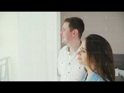 A man and a woman are standing in front of the window, he kisses her