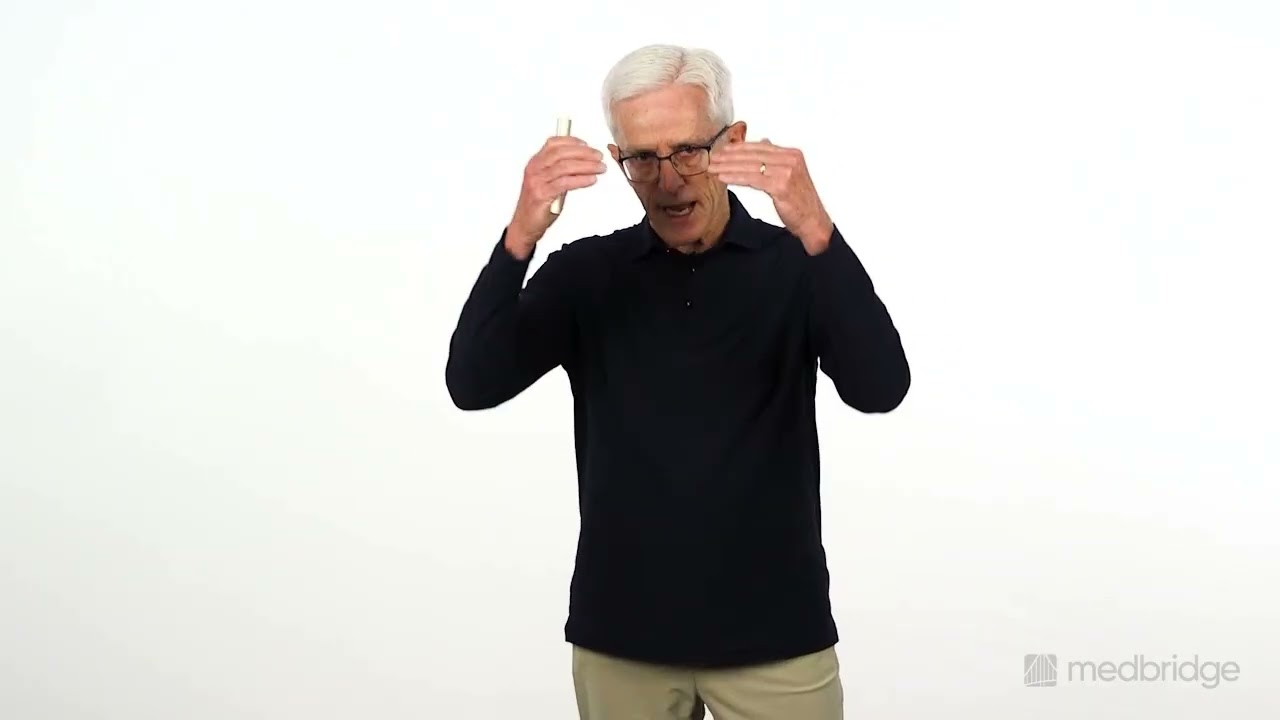An older man with white hair and glasses gestures with both hands in front of a white background.