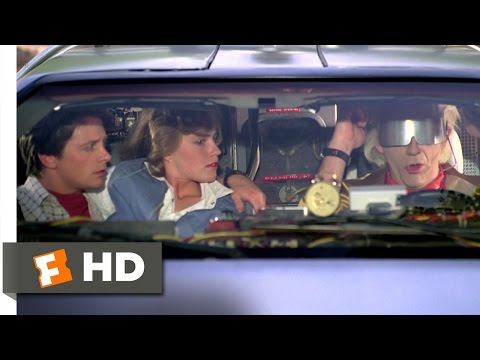 Back to the future DeLorean car with characters played by Michael J. Fox, Elisabeth Shue and Christopher Lloyd sat in the front. Christopher Lloyd is dressed as mad professor 'Doc' Brown and is wearing a futuristic silver sunglasses visor.