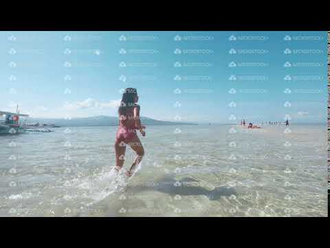 Asian girl is running in ocean water on sand beach in slow motion, back view.