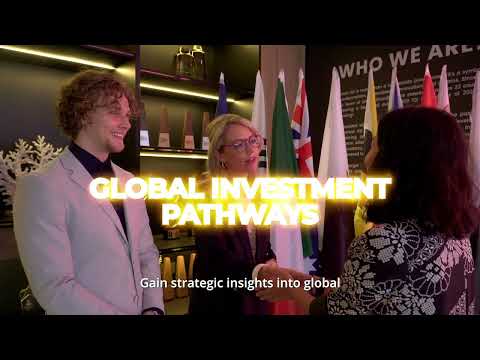 A man in a beige suit and blue tie stands in a modern office lobby with wooden floors, colorful chairs, and soft lighting