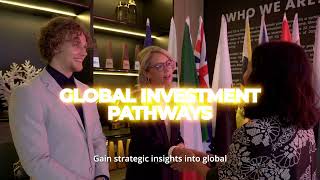 A man in a beige suit and blue tie stands in a modern office lobby with wooden floors, colorful chairs, and soft lighting