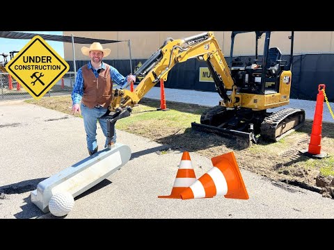 Construction site scene with a CAT excavator, a smiling worker in a hat and vest, an 'Under Construction' sign, and orange safety cones near a large golf-ball on a tee.