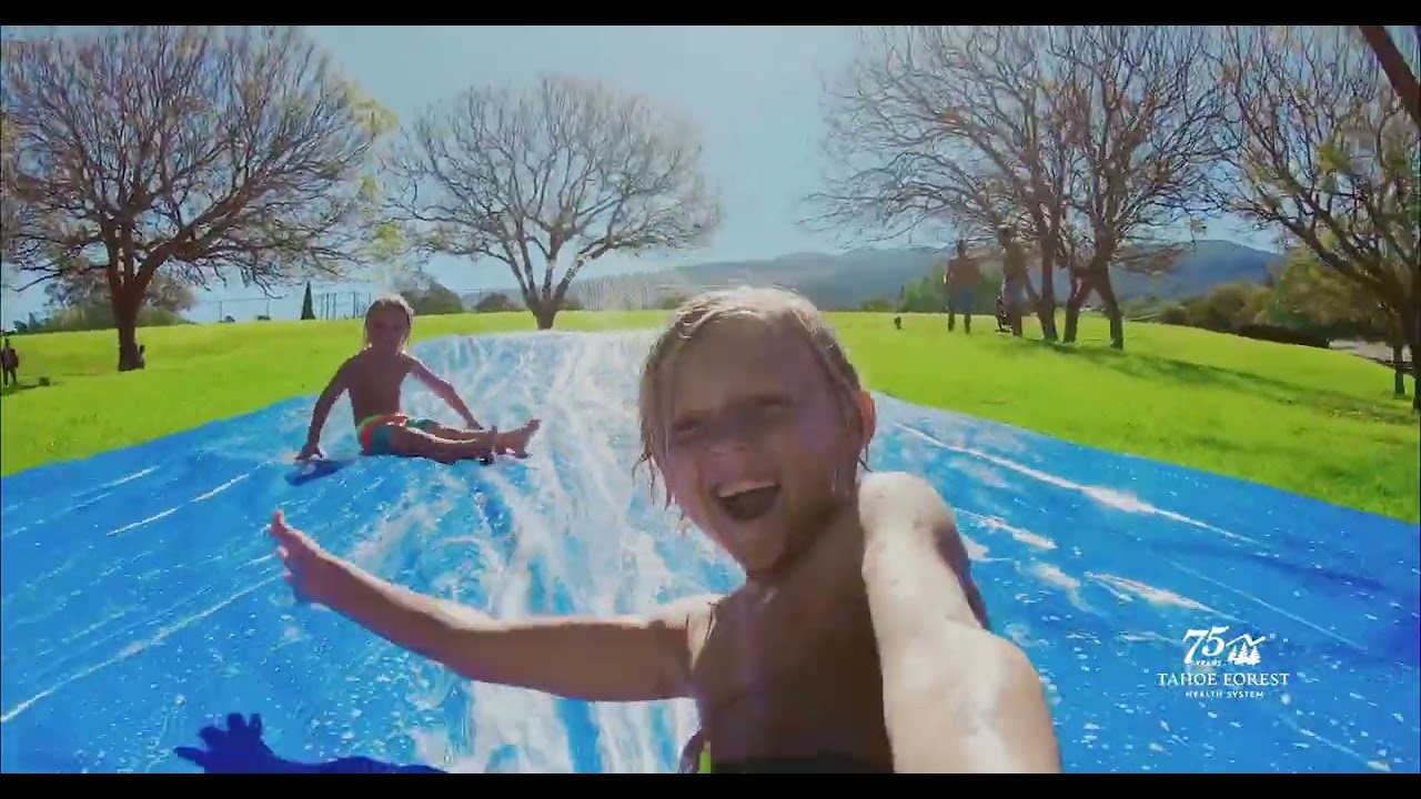 Two boys having fun on a slip-and-slide on a bright green lawn with trees