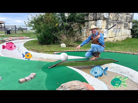 Man in a cowboy hat kneels on a mini-golf green, pointing at a white ball with a putter; cartoon fish decorate the course.
