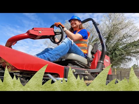 Smiling worker in a blue hard hat and orange safety vest driving a red ride-on lawn mower outdoors.
