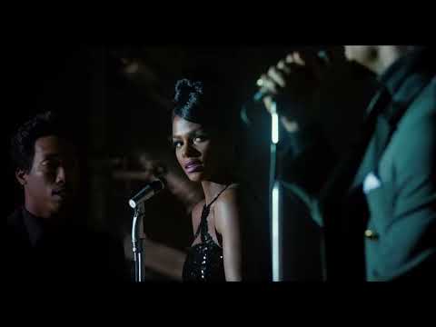 Trailer still with spotlighted mic and band risers, evoking James Brown’s stagecraft and tight band cues