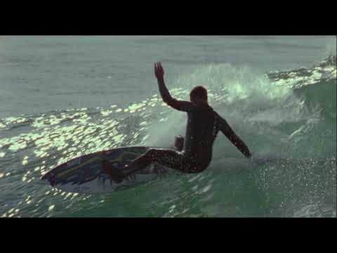 Trailer frame of a surfer dropping into a steep face under golden light