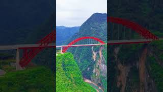 Red Steel Arch Spans Deep Valley, Aerial Panorama Of Mountain High Arch Bridge