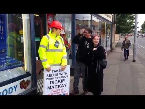 Dickie the mannequin outside the shop with a couple having a selfie taken mannequin-man performming as a Mechanical Mannequin: Taking the place of Dickie Mackay, the mannequin that has been standing outside Mackays of Cambridge for years. Passers-by got a shock when taking a selfie with the mannequin, when he suddenly comes to life.
In this one a couple get a shock as Dickie the mannequin moves. for Mackays on 23/08/2014