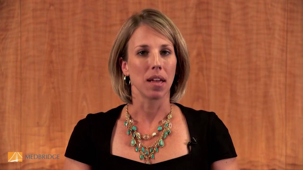 A blonde person in a black top and colorful necklace discusses digital healthcare with Medbridge logos in the corners against a wooden background.