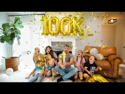 Family celebrating a milestone at home with large gold '100k' balloons and shower of confetti.