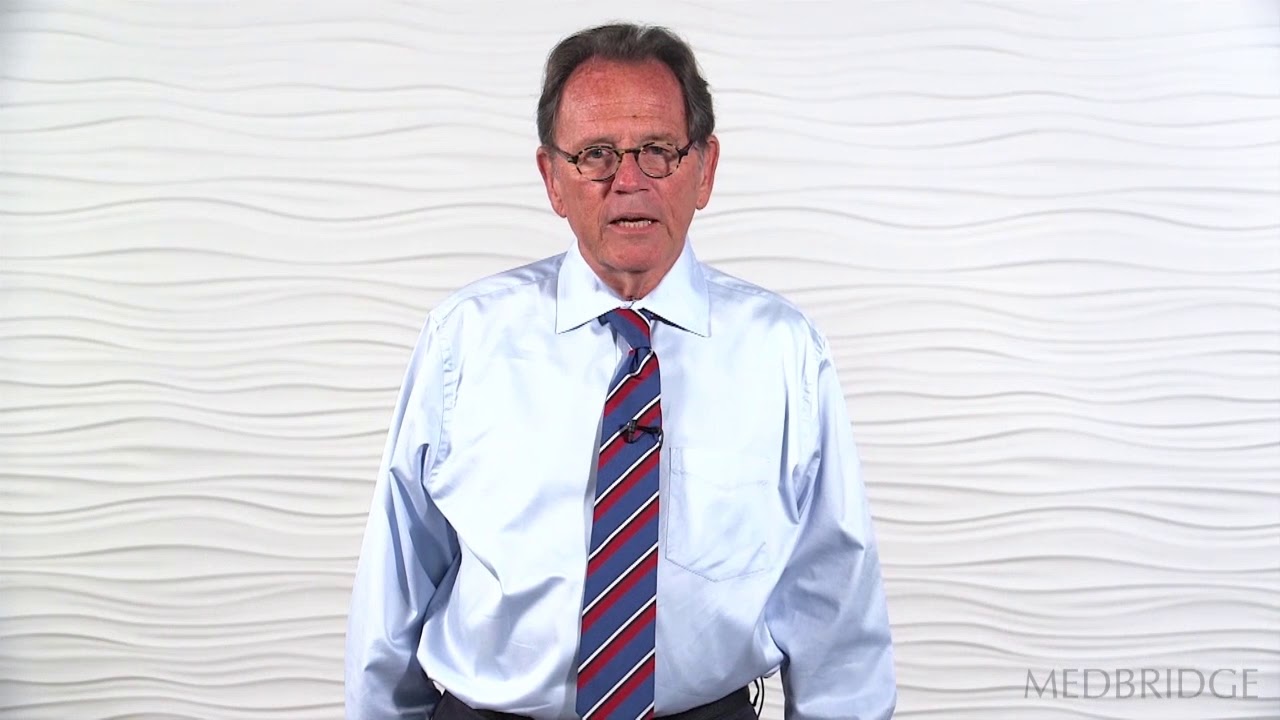 A man in professional attire stands against a textured wall, representing Medbridge's healthcare education.