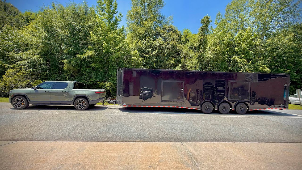 Rivian R1T electric pickup towing a massive triple-axle trailer on a country road