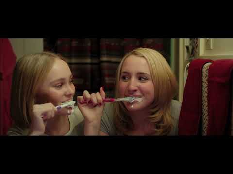 Trailer still of the Colleens mic’d up on a small stage, colored lights flaring