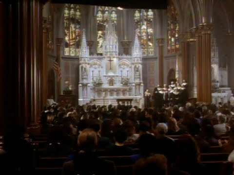 Trailer frame: the choir in full voice during a televised mass, matching the soundtrack’s finale energy