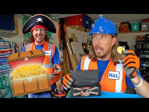 Two men in safety vests in a workshop, one wearing a pirate hat and the other a blue hard hat, with a cartoon treasure chest of gold coins in front.