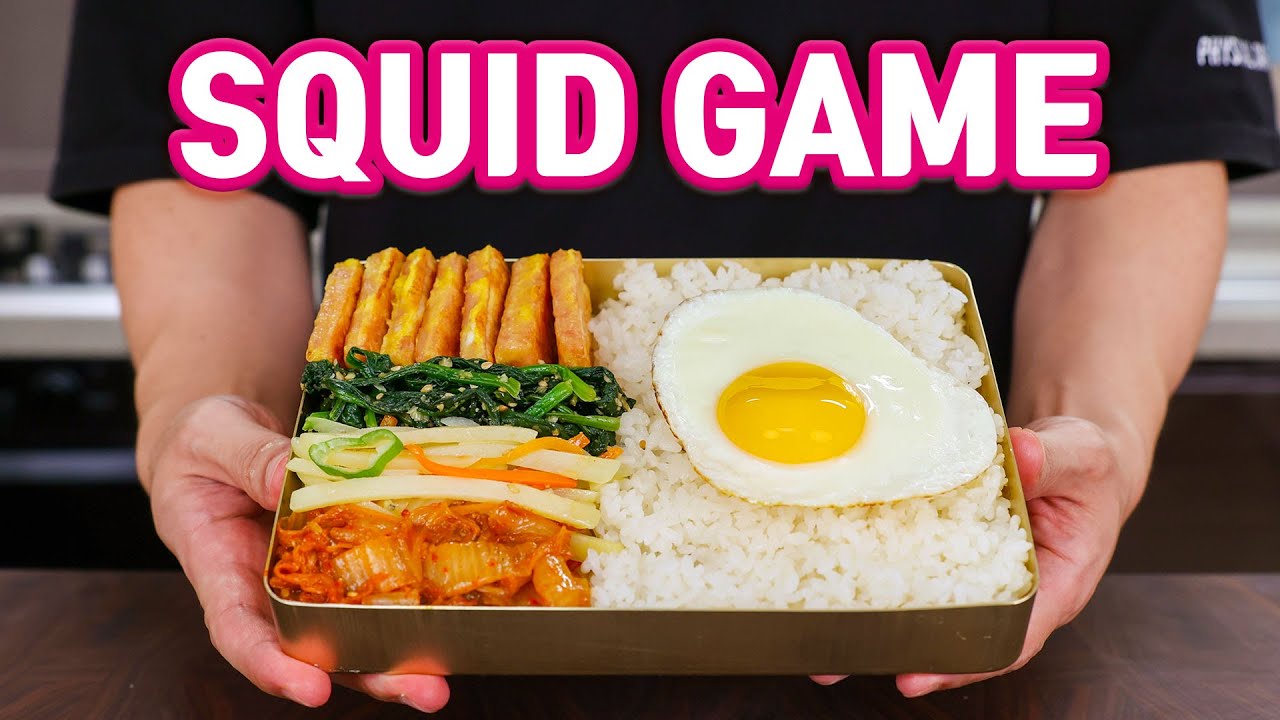A Squid Game style Korean dosirak lunchbox arranged with rice four Korean banchan side dishes and a fried egg in the iconic compartmentalized container