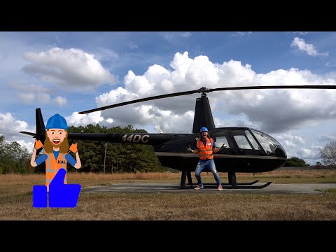Person in orange safety vest and blue hard hat posing beside a black helicopter on a grassy airfield; cartoon worker illustration giving a thumbs up on the left.