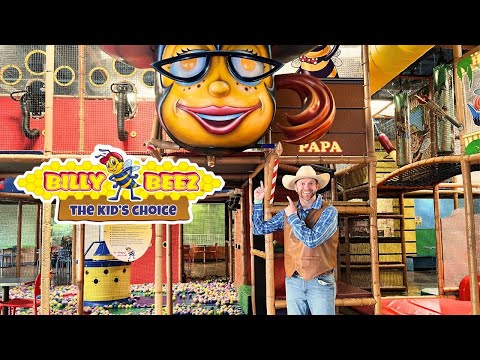 Man in a cowboy hat and vest points at a colorful Billy Beez play area sign inside an indoor kids' attraction park.