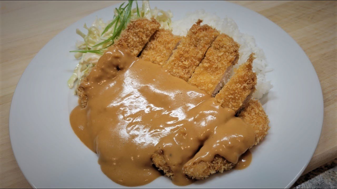 A close up of crispy golden Korean donkkaseu pork cutlet being cut with a knife revealing the tender meat inside and the crunchy breaded exterior
