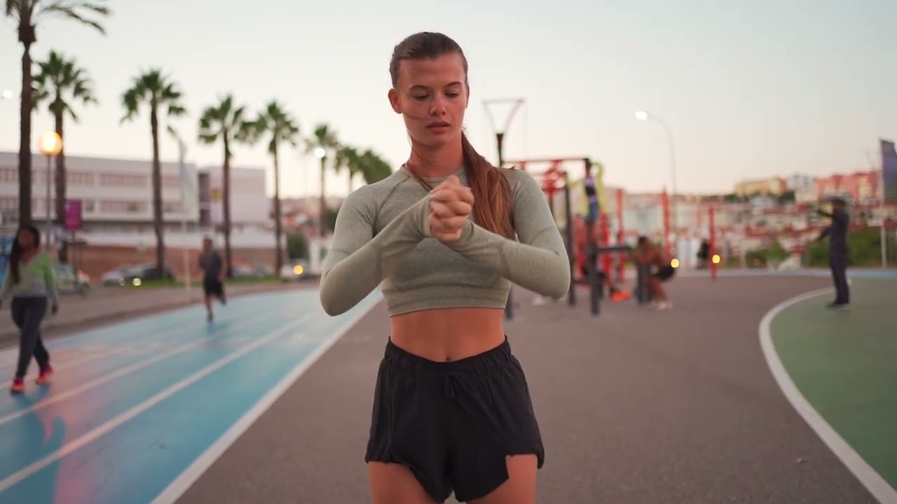 Female athlete stretching on a track at dusk.