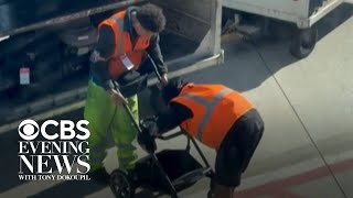 Bystanders cheer for baggage handlers after they finally fold baby stroller