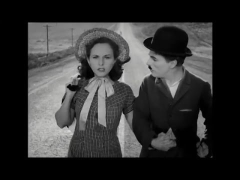 Charlie Chaplain and a woman in a a bonnet walking down a long straight dusty country road.