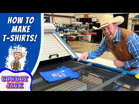 Man wearing a cowboy hat and vest demonstrates screen printing a blue T-shirt on a large press in a workshop, for a tutorial video.