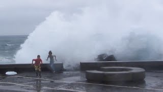 Boys running for huge hurricane waves at Sao Miguel, Azores