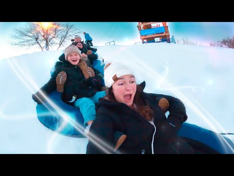 Kids sledding down a snowy hill on a blue inflatable tube, laughing and bundled in winter gear.