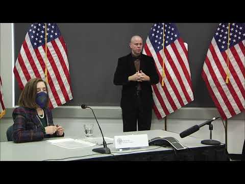 Governor Brown holding a mask with a sign language interpreter behind her.