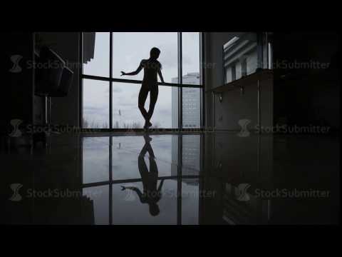 Silhouette of a ballerina by the window. A young girl ballet dancer at the window is reflected in
