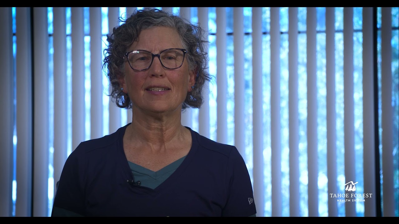 Dr. Johanna Koch sitting and speaking in front of a window with vertical blinds.