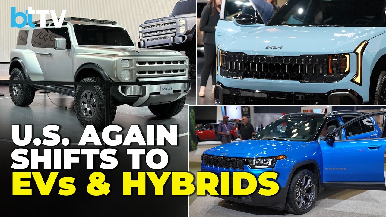 New York International Auto Show floor with automaker displays and reporters covering EV and hybrid industry trends