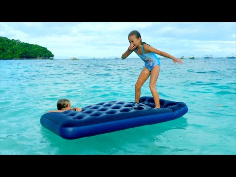 Children swim and dive in the sea on the beach with a mattress