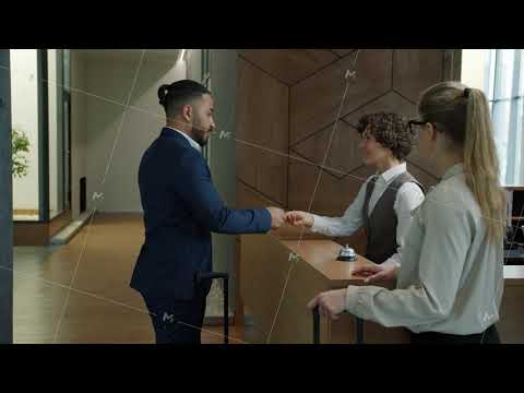 Arab businessman paying for hotel room with smartphone talking to receptionist then walking with