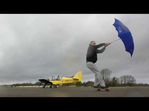 Skateboarder with umbrella pulled FAST by strong wind