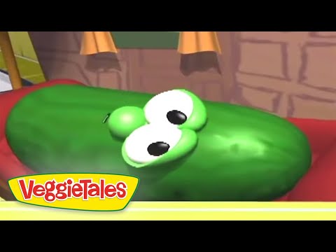 Green cucumber character with big white eyes lying on its side in a VeggieTales scene.