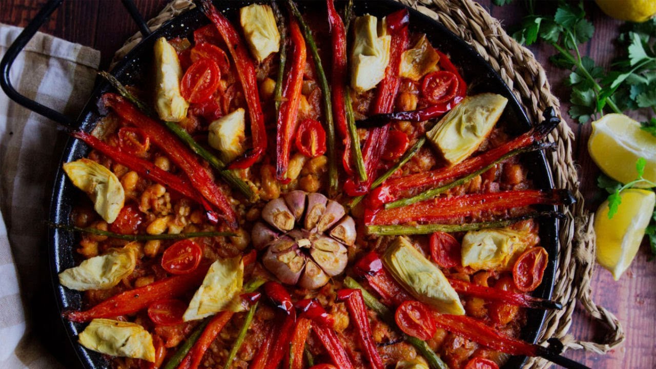 A large pan of vegan arroz al ahorno sits garnished with roassted pepper and garlic