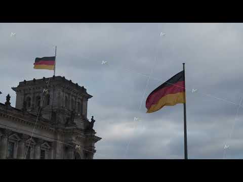 National flags at historic German parliament building. Flown symbols against cloudy sky. Berlin