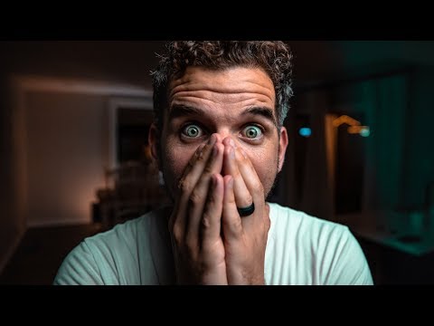 Man with wide eyes covering his mouth with both hands, surprised expression in a dimly lit room