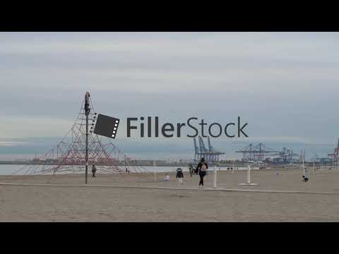 Kids playing on beach and climbing rope net. Shore view with cranes, Valencia