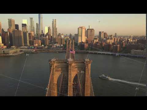 AERIAL: Flight over Brooklyn Bridge with American flag waving and East River view over Manhattan New