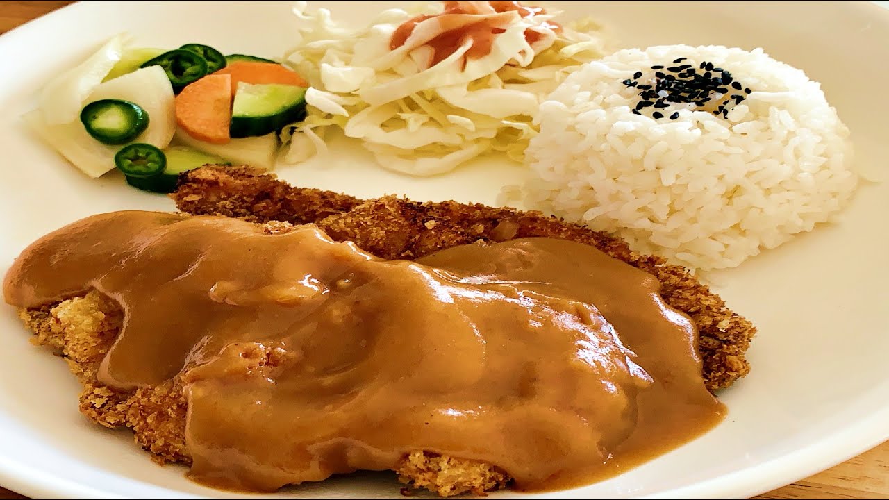 A small dish of Korean donkkaseu sauce being poured over a sliced golden pork cutlet showing the glossy brown sauce coating
