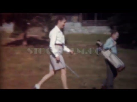 1945: Man caddy woman golfer carries golf clubs bag down fairway. TRYON, NC