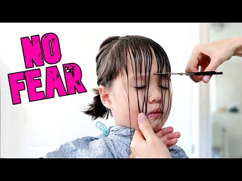 Little girl with bangs being trimmed with scissors, wearing a hair cutting cape, and text overlay saying "NO FEAR," illustrating a tutorial on trimming children's bangs.